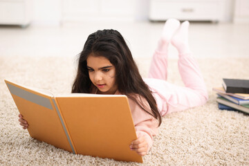 Naklejka premium Cute little girl reading book on floor at home