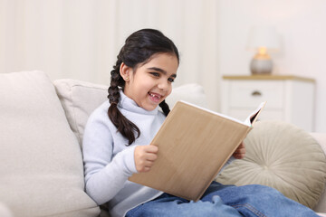 Naklejka premium Cute little girl reading book on couch at home
