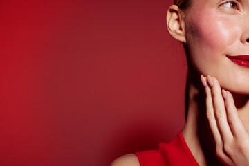 Fototapeta premium Close-up of a woman with red lipstick and red dress touching her face against a red background. Concept of beauty, makeup, fashion, and elegance with vibrant colors.