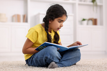 Naklejka premium Cute little girl reading book on floor at home