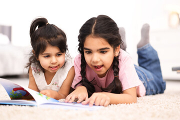 Naklejka premium Cute little girls reading book together at home