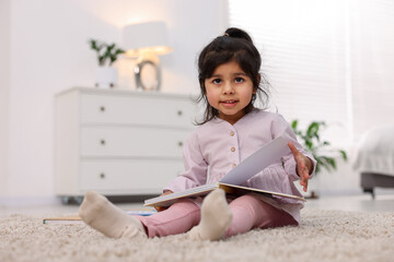 Naklejka premium Cute little girl reading book on floor at home. Space for text