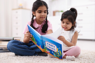 Naklejka premium Cute little girls reading book together at home