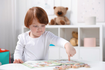 Cute little boy playing with toys at white table indoors