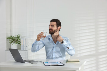 Naklejka premium Man with glass of water suffering from heat at table near white wall indoors