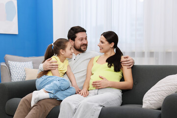 Pregnant woman, her husband and daughter on sofa at home