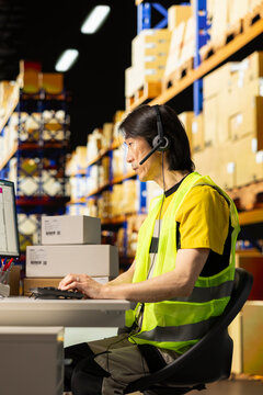 Call center male worker answer help line calls in a logistics warehouse, updating clients on orders and resolving cargo mix ups. Managing shipping software tied to barcodes and airway bills.