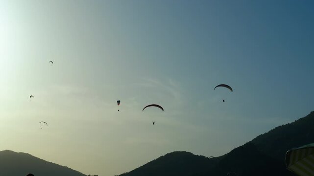 Paragliders flying over green hills at sunset. Silhouetted paragliders drifting peacefully across golden evening sky, gliding above verdant rolling hills with sunset illuminating colorful landscape
