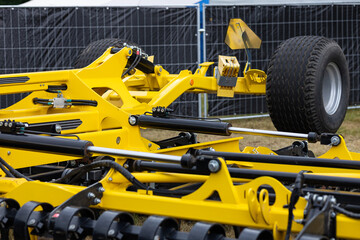 Fototapeta premium Modern yellow agricultural cultivator being prepared for spring field work in a farm workshop. Maintenance of hydraulic systems and disc harrows to ensure high crop yield and profit