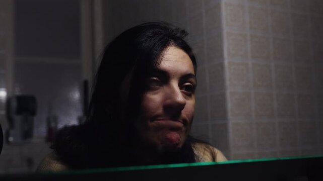 Woman staring at reflection in bathroom mirror at night, weary expression capturing fatigue, self doubt and quiet confrontation with aging