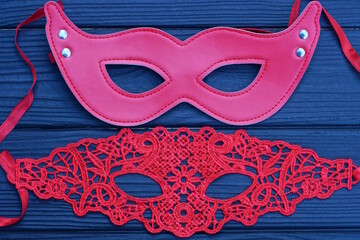 A set of two red leather and fabric masks lie on a black wooden table