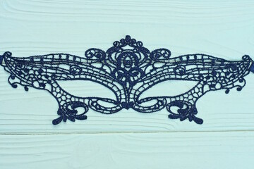 one black lace fabric mask lies on a yellow wooden table