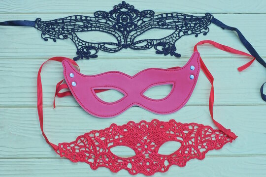 A set of three black and red masks lie on a yellow wooden table