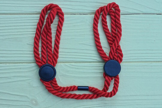 Handcuffs made of red cord with black plastic fasteners lie on a yellow wooden table