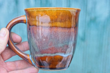 hand holding one big brown ceramic cup on green background