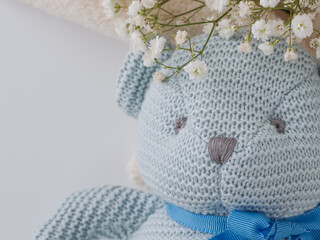 Closeup pastel blue crocheted teddy bear on beige fleece blanket with baby’s breath flowers. Soft newborn flat lay for baby boy announcements, showers, nursery branding © Andrea
