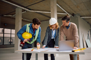 Real estate developer analyzing blueprints with architect and worker at construction site.