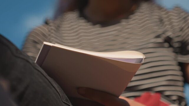 Low angle notebook against sky, aspiring writer sketches ideas, poet captures sunset verses, traveler logs sights, illustrator traces quick thumbnails blue sky backdrop, striped shirt, soft breeze,