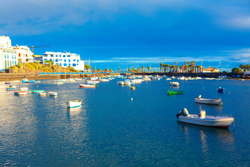 Arrecife town in Lanzarote, coastal harbor with anchored boats on blue water, framed by white buildings and palm-lined shores. Clear skies and calm reflections create travel and lifestyle concept © Leilani