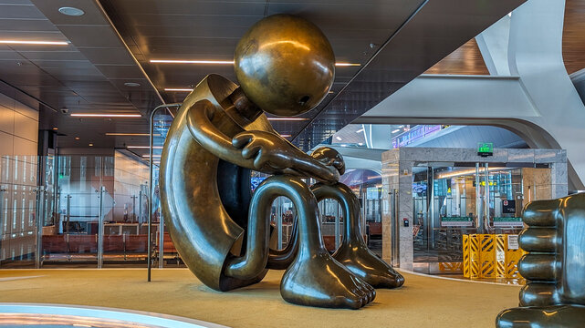 Doha, Qatar, March 17, 2024. Interior view of Doha Hamad International Airport shows one large human figure bronze sculpture bending and sitting on the ground at airport lounge.