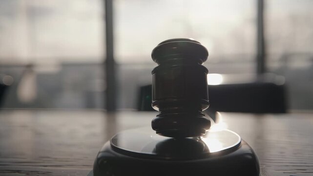 Close-up of a judge's gavel on a wooden table with blurred courtroom background.