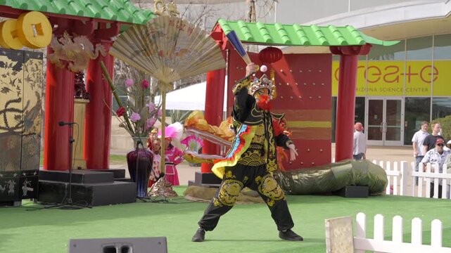This slow motion video shows a traditional face changing Chinese dancer performing on an outdoor stage. 
