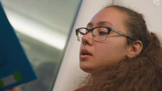 Lady reads aloud. Passenger softly recites on train. Focused female traveler narrates during railway journey. Woman with curly hair concentrates and recites words quietly on moving train