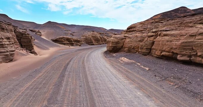 Aerial view of a winding gravel road through dramatic layered Yardang formations in the remote desert of Xinjiang, China.