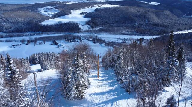 A snow-covered chairlift and powder runs wind through a densely wooded mountain valley in a serene winter landscape. Mont-Castor, Gasp&eacute; Peninsula, Matane, Quebec, Canada. Winter 2026.