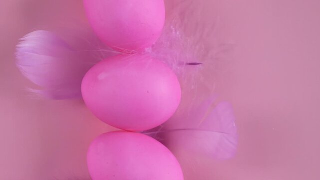 A row of pink Easter eggs and purple feathers on a pink background.Traditional Easter celebration concept, seasonal decoration and holiday background.