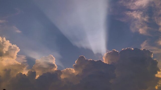 Divine sun rays or God rays breaking through dramatic white clouds in a blue sky.