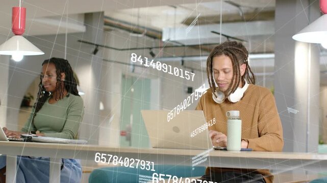 Two people typing at laptops on table in tech hub, starting animated data overlays streaming down