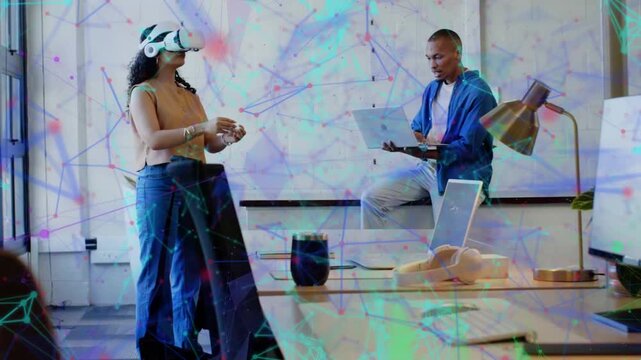 Woman in VR headset reaching forward, selecting AR visuals while man typing laptop for tech demo