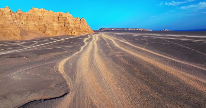 Aerial view of winding tire tracks through the sandy desert featuring a spectacular golden Yardang formation in Xinjiang, China.
