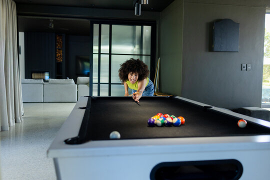 African American woman leaning aiming over pool table with cue in home game room wearing lime-top