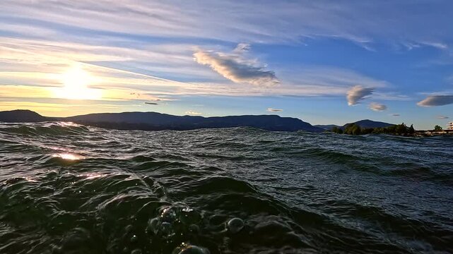 Panning shot of lake waves at sunset with dramatic cirrus clouds in blue sky, at times under water.
