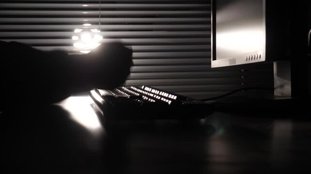 Worker silhouette expressing anger and frustration by hitting a keyboard in a dark office at night, symbolising stress, overwork, and exhaustion from long hours and tight deadlines