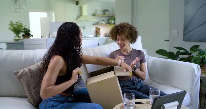 African American women on couch placing box, cutting tape, revealing bubblewrap item for inspection