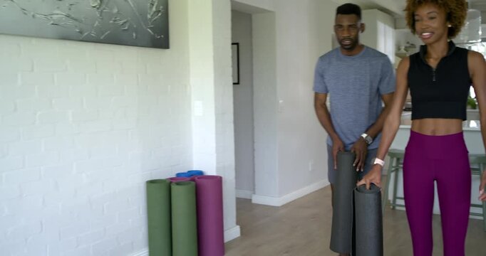 African American couple entering with mats in gymwear, adjusting phone rig, starting workout stream