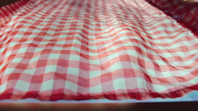 Red gingham curtain fabric moving gently near window glass, detailed view of patterned textile inside rustic mountain chalet