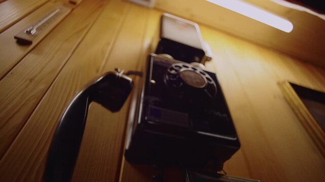 Hand placing receiver back onto vintage rotary wall telephone inside wooden chalet interior, retro communication device mounted on rustic paneling