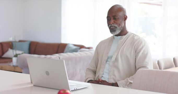 African male senior getting call waving and greeting contact at home with silver laptop, copy space