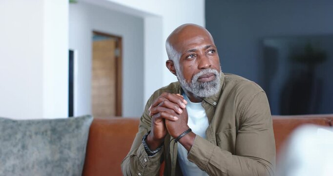 African man shifting from thoughtful to smiling while noticing camera on brown couch, living room