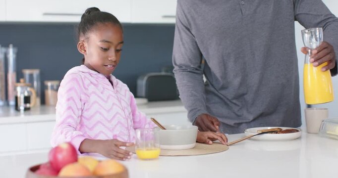 African American father-daughter pouring juice after nudging plate, daughter steadying bowl  and  gl