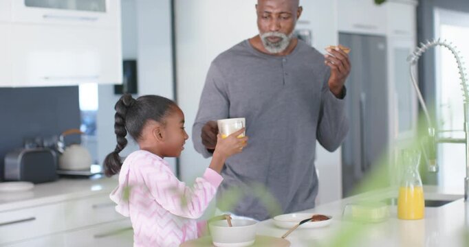 African American man and child offering orange juice man hovering mug playfully in kitchen sipping