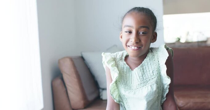 Preteen girl sitting on brown sofa by window in green top, camera catching eye, turning smiling