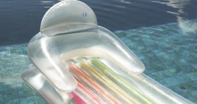 Clear pool lounger is bobbing, drifting on tiled ledge as breeze ripples move it, tubes glinting