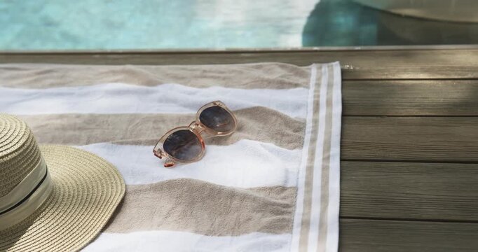 Camera panning and zooming is bringing clear shades closer on striped towel to show poolside calm