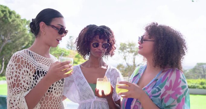 Female friends looking at drinks, standing poolside holding glasses with citrus, celebrating
