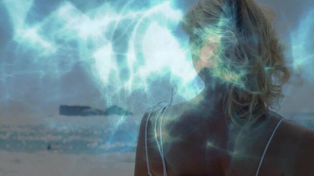 Woman at shore, luminous overlay flowing across face, causing turning and fixing hair for fashion
